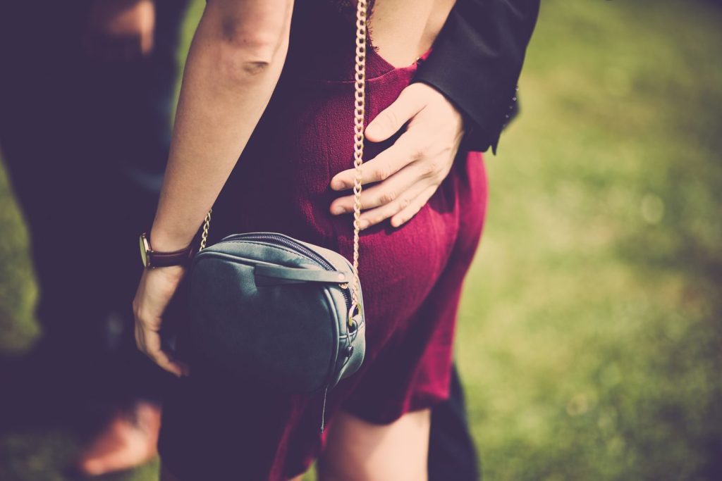 A stylish woman in a red dress with a handbag enjoys a romantic moment outdoors.