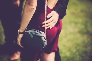 A stylish woman in a red dress with a handbag enjoys a romantic moment outdoors.