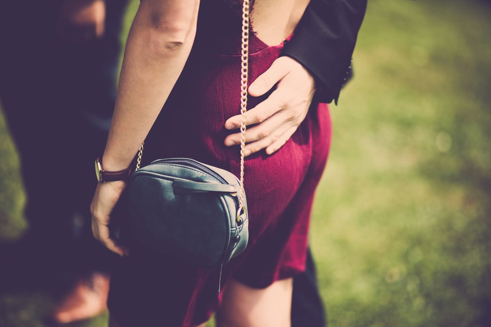 A stylish woman in a red dress with a handbag enjoys a romantic moment outdoors.